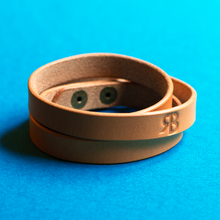 Load image into Gallery viewer, Full-grain brown leather triple-wrap bracelet with an &#39;RB&#39; logo on a blue background, clasped