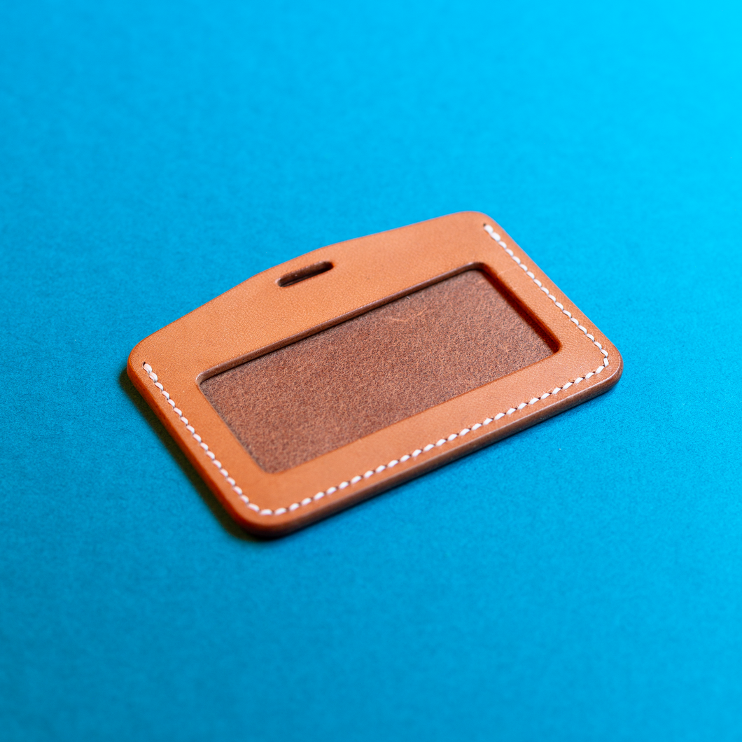 Full-grain hand-stitched brown leather ID card holder on a blue background