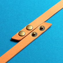 Load image into Gallery viewer, Full-grain brown leather triple-wrap bracelet with antique brass snaps on a blue background, unclasped