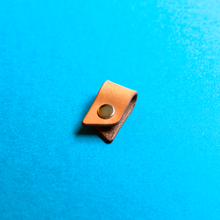 Load image into Gallery viewer, Brown leather strap clip with a metal button on a blue background, closed