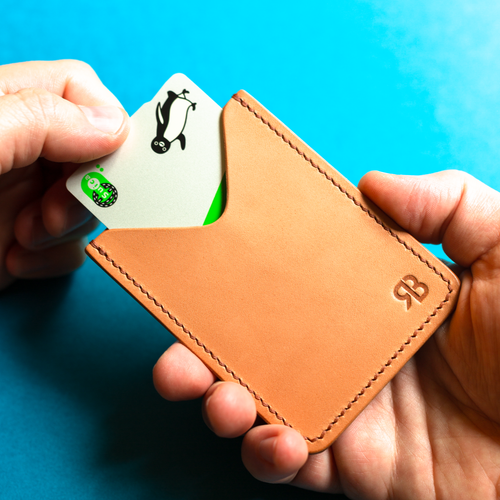 Full-grain hand-stitched brown leather cardholder with a card featuring a penguin design against a blue background, front