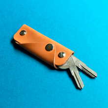 Load image into Gallery viewer, Full-grain brown leather key holder with keys on a blue background