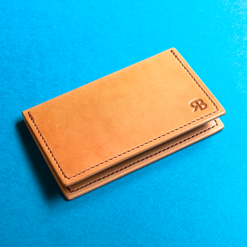 Full-grain hand-stitched brown leather business card case with an 'RB' logo on a blue background, outside